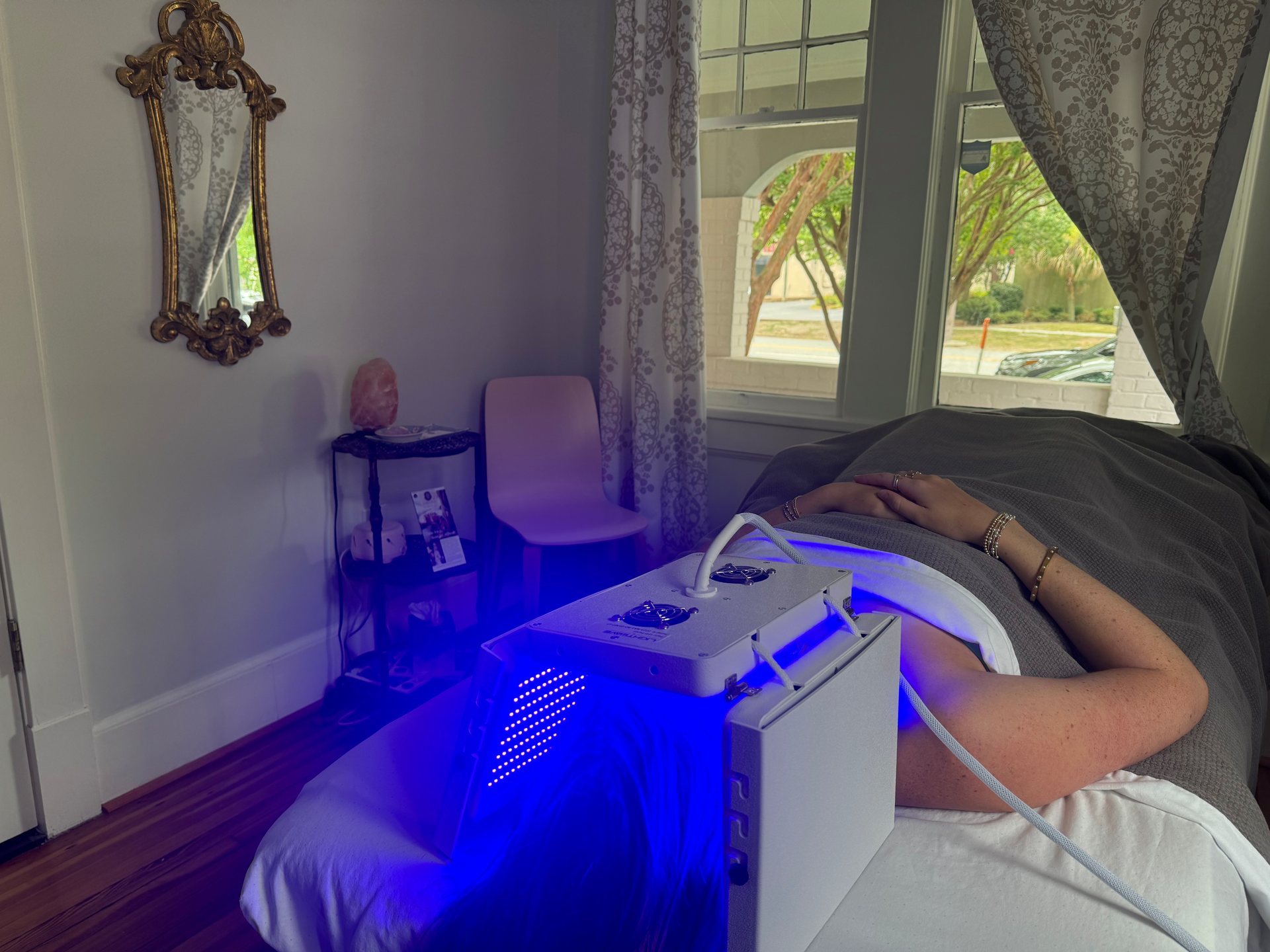 A woman is laying on a bed with a blue light on her back.