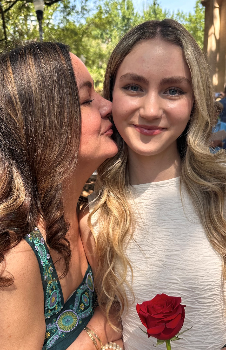 A woman is kissing another woman on the cheek while holding a red rose.