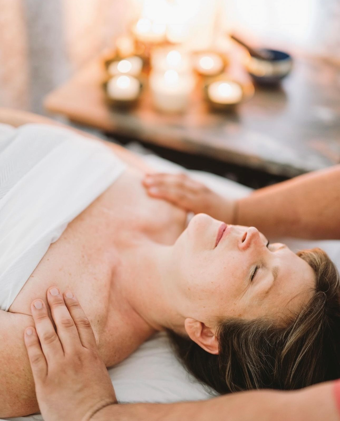 A woman is getting a massage in a spa with candles in the background.