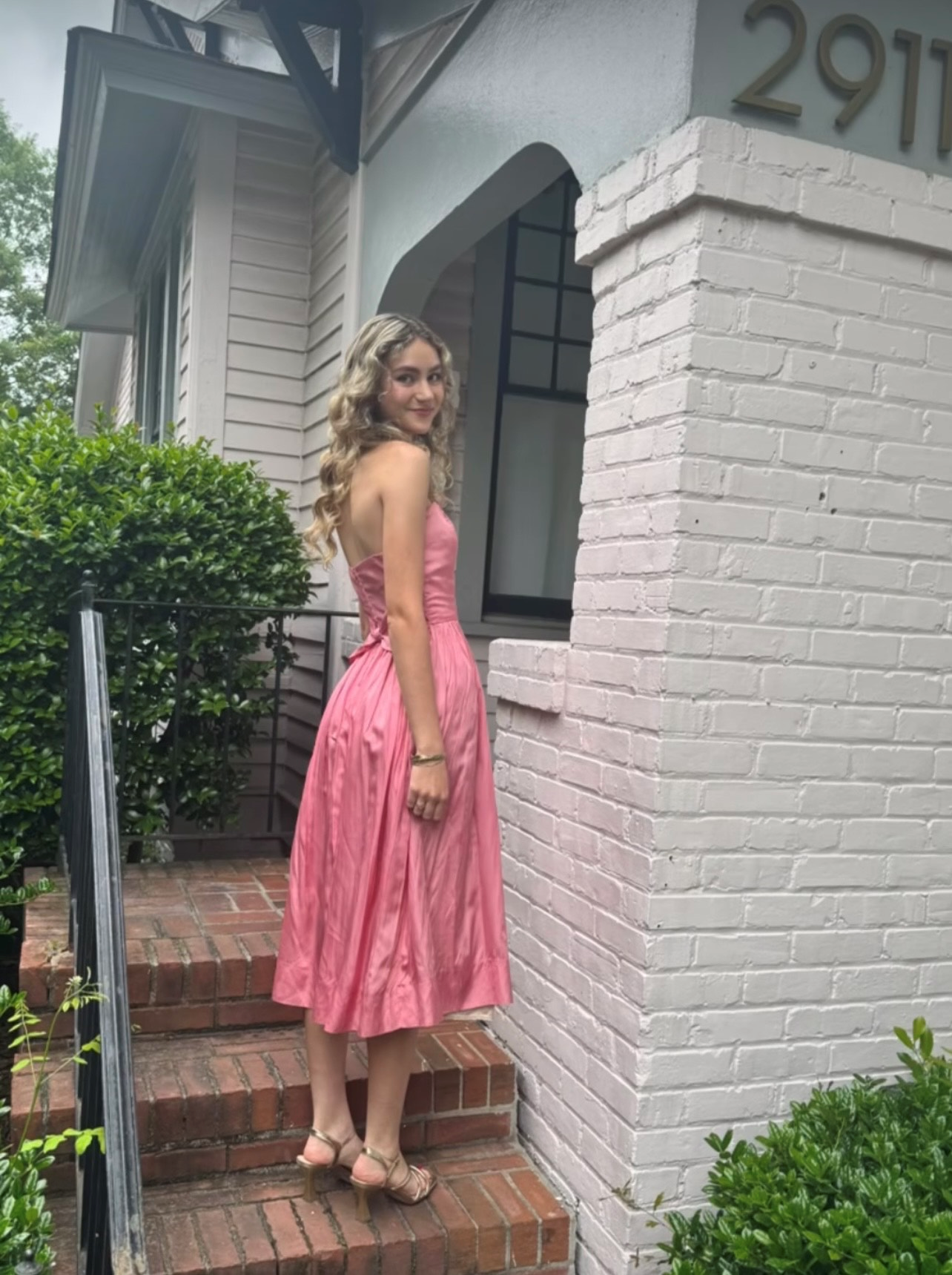 A woman in a pink dress is standing on the steps of a house.