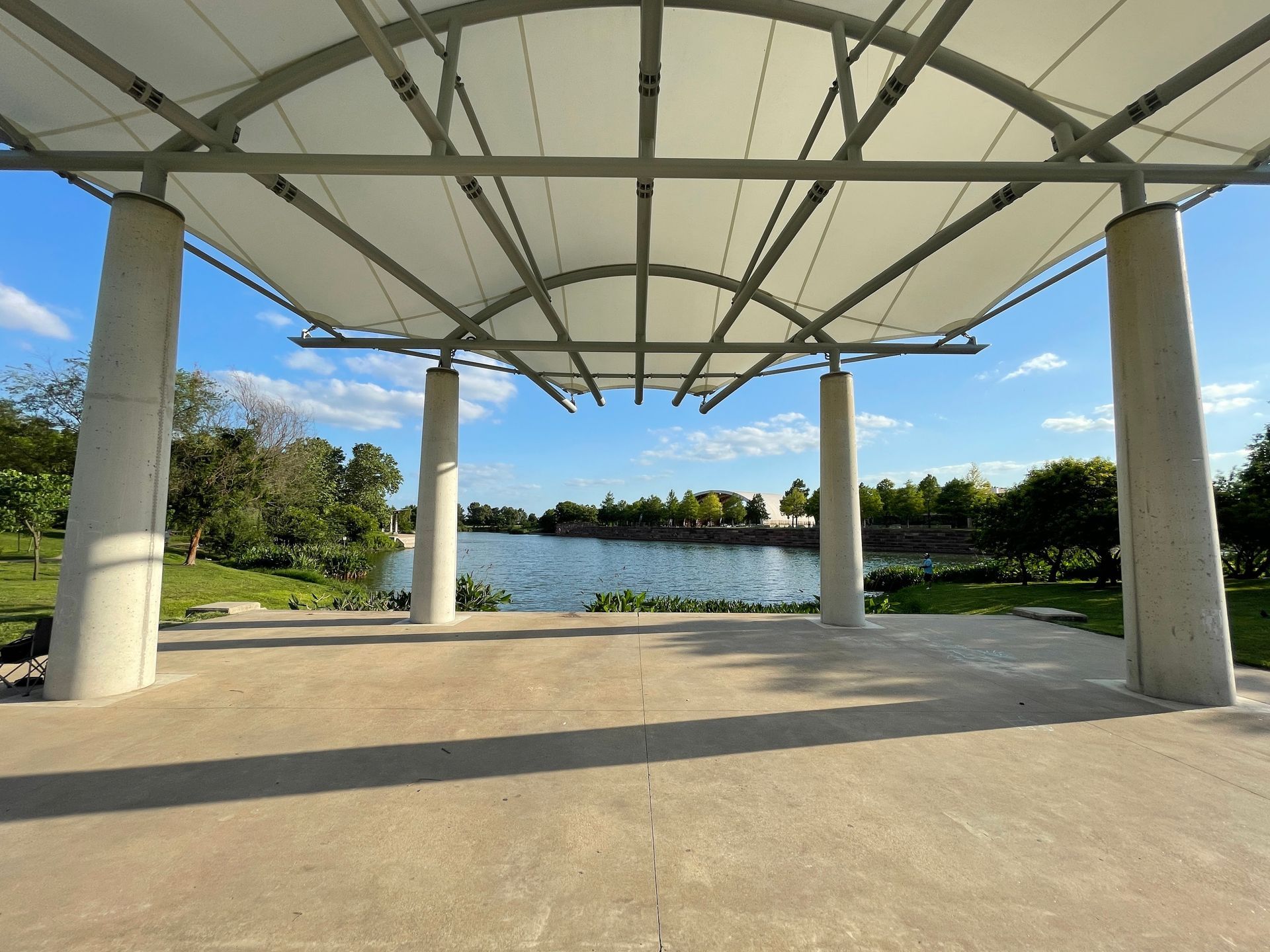 Stage with white canopy, overlooking a lake under a blue sky.