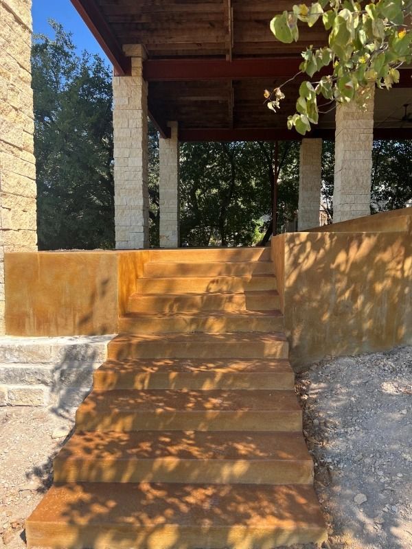 Outdoor stairs with rust-colored steps lead to a covered porch with stone columns.