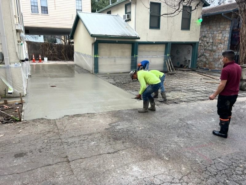 Construction workers leveling wet concrete for a driveway next to a garage.