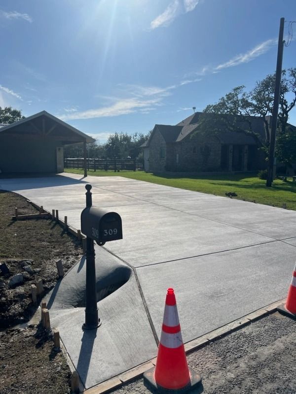 Newly poured concrete driveway with attached carport and house in background under a blue sky.