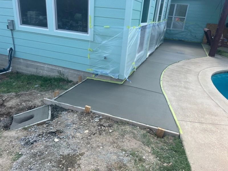 Newly poured concrete walkway next to a turquoise house and swimming pool.