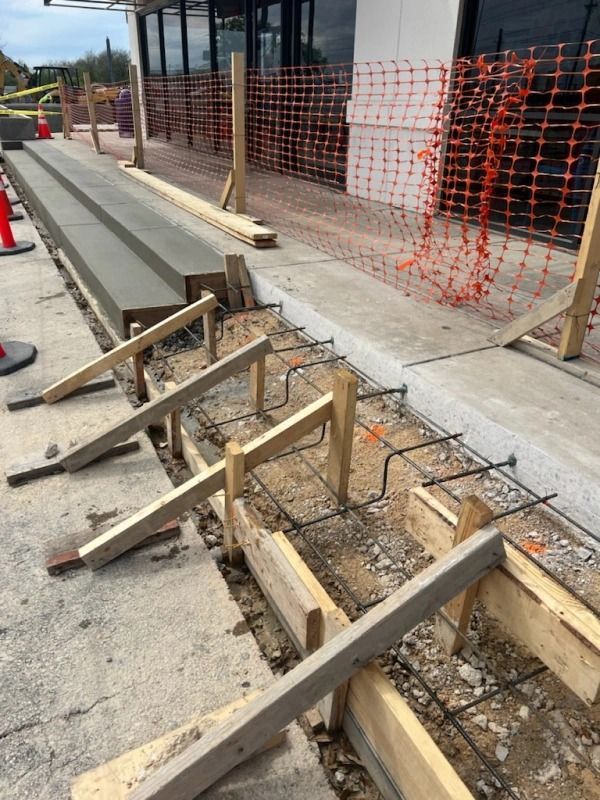 Construction site: Concrete forms with rebar in foreground, completed concrete steps in background.