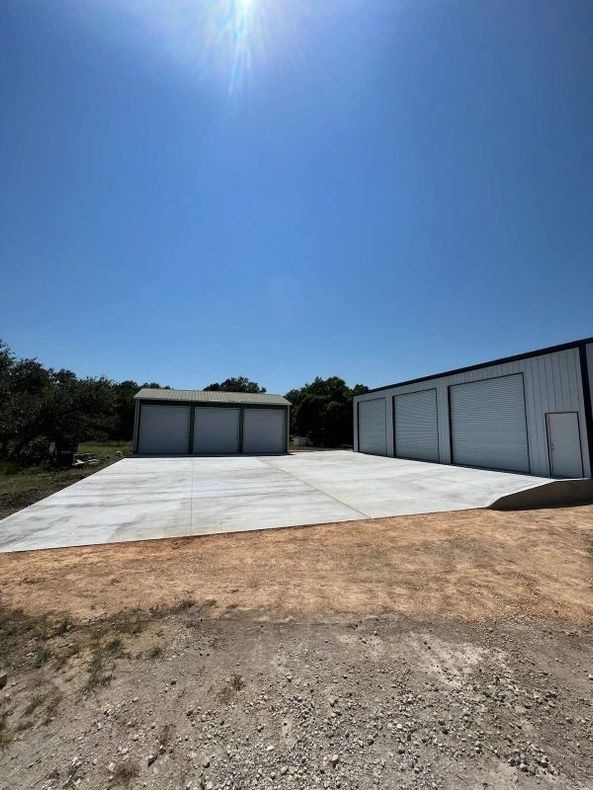Two metal storage buildings with concrete pad on a sunny day, blue sky.