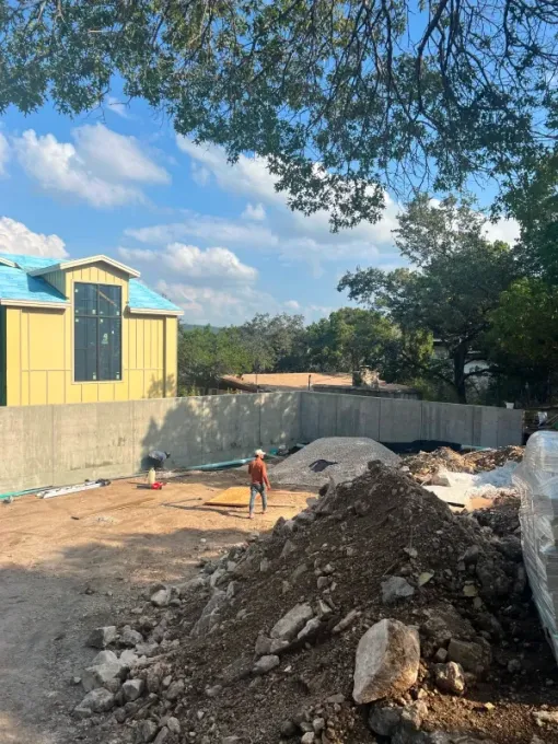 Construction site: a person in a hard hat stands before a concrete wall and a building with a yellow facade.
