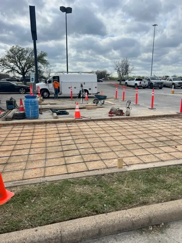 Construction site: Concrete grid laid, with truck, cones, and workers, in a parking lot.