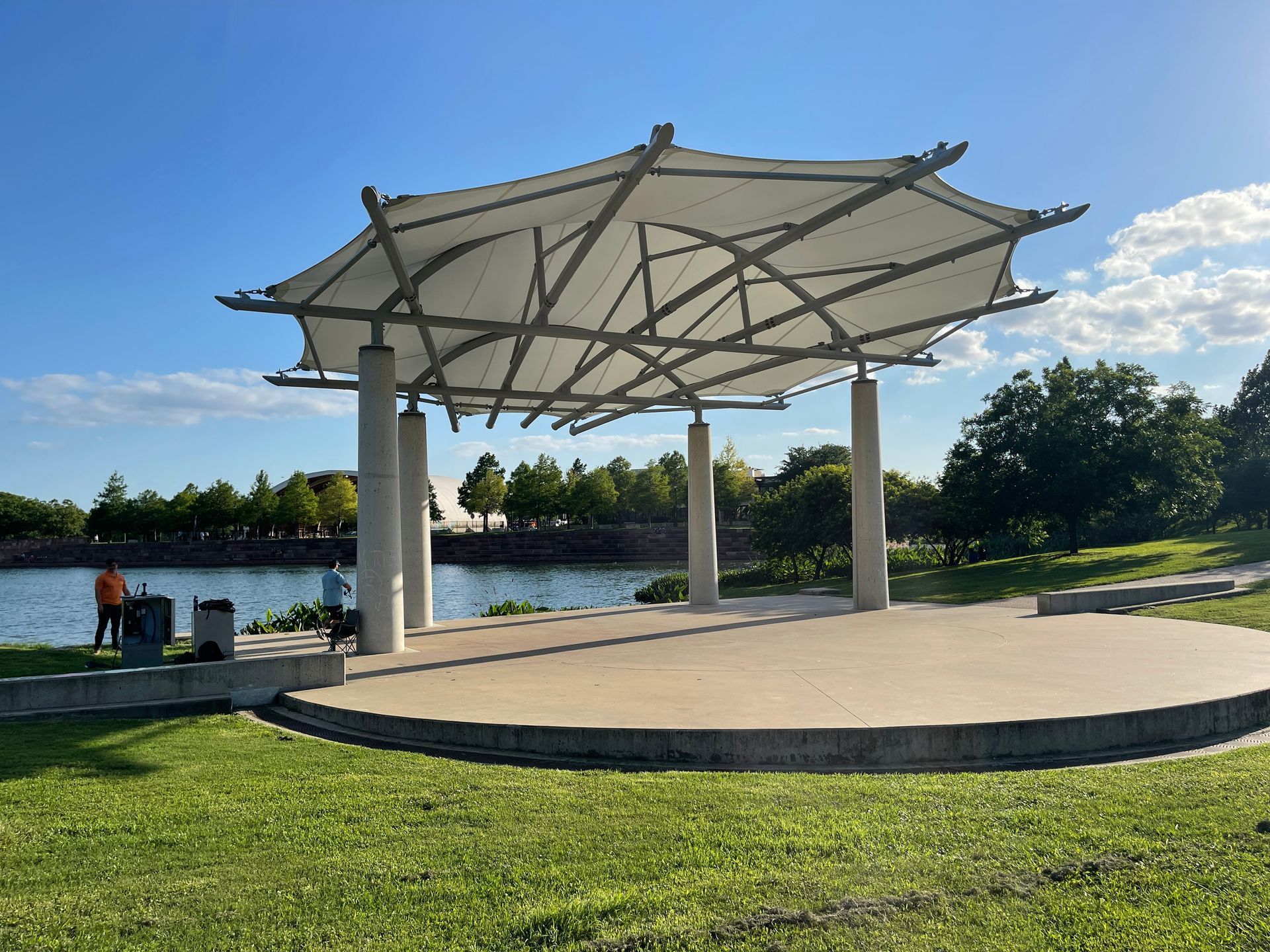 Pavilion by water with white canopy and concrete stage on a sunny day.