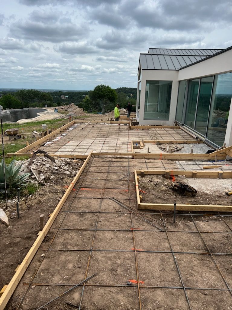 Construction of a concrete patio with rebar grids, near a modern house and landscape in progress, outdoors.