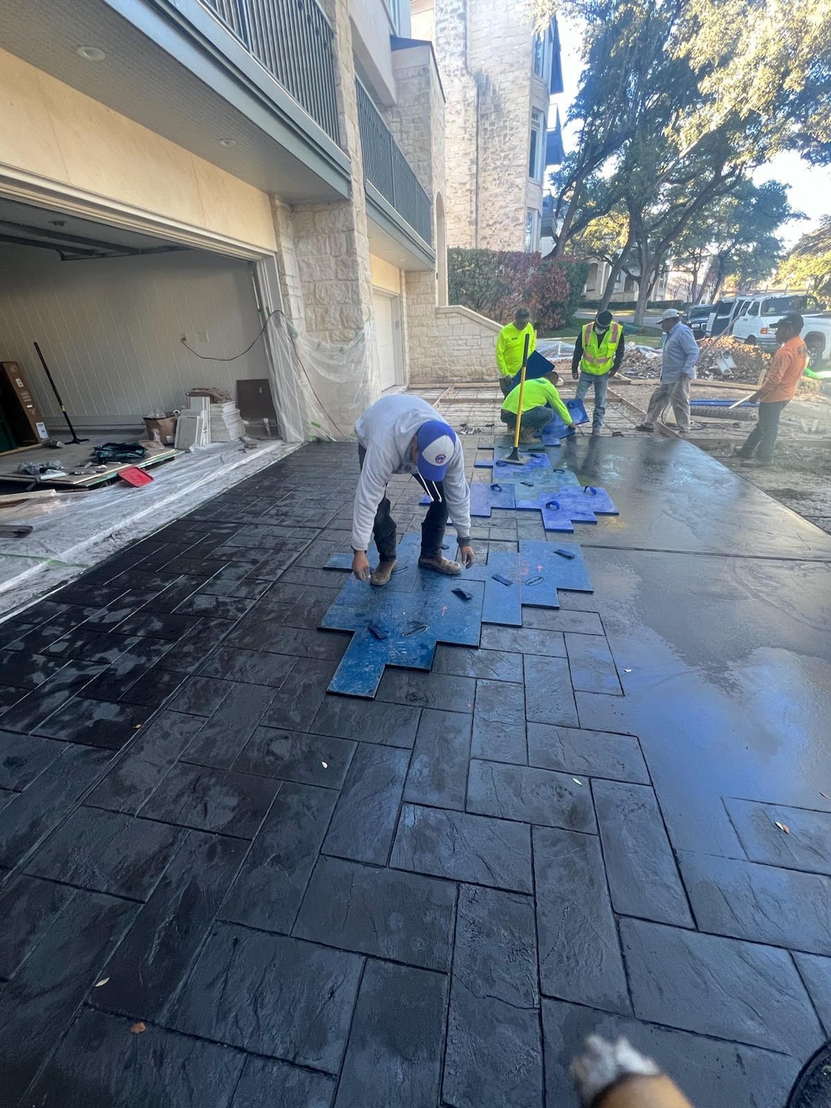 Workers laying textured pavement stones in front of a building with an open garage.
