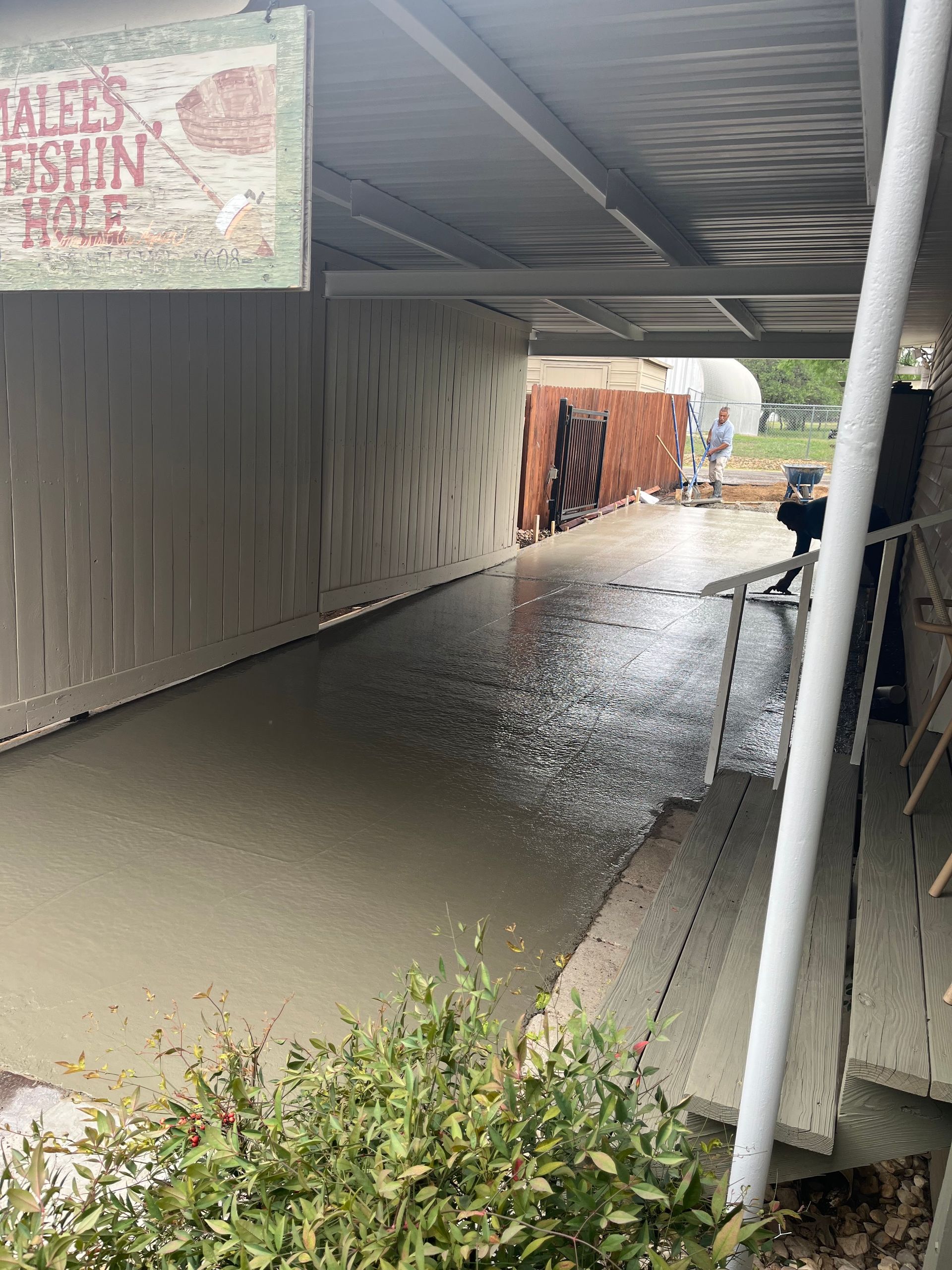 A wet concrete walkway under a porch roof with fencing on both sides, a sign, and steps.
