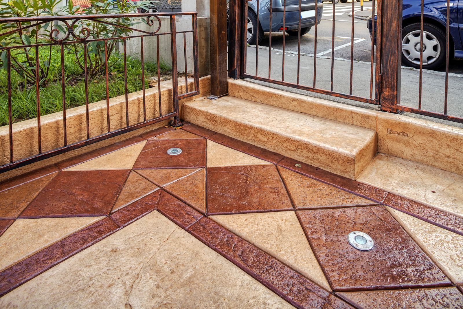 Decorative concrete patio with geometric patterns in brown and beige, with a metal railing and stairs.