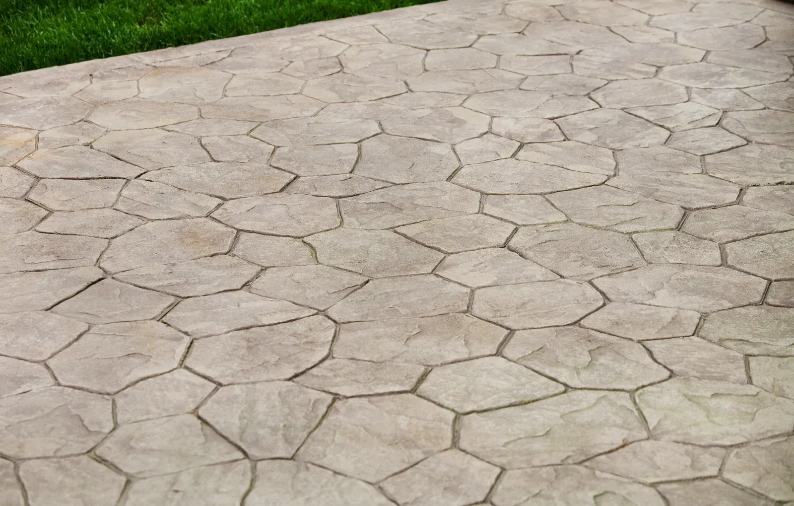 Textured, stamped concrete patio with irregular, stone-like pattern and green grass border.