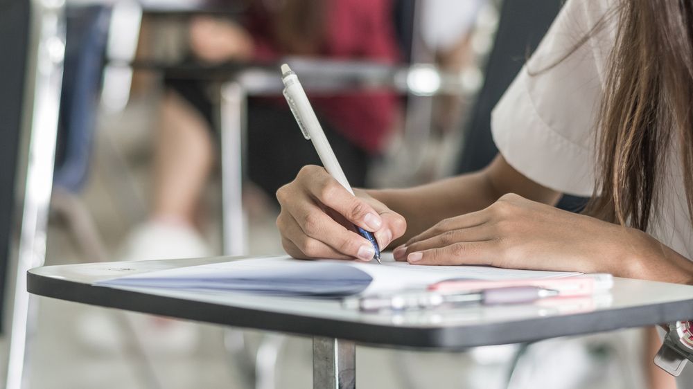 A Woman is Sitting at a Desk Writing on a Piece of Paper With a Pen — Switch Gear Automotive in Riverstone, NSW