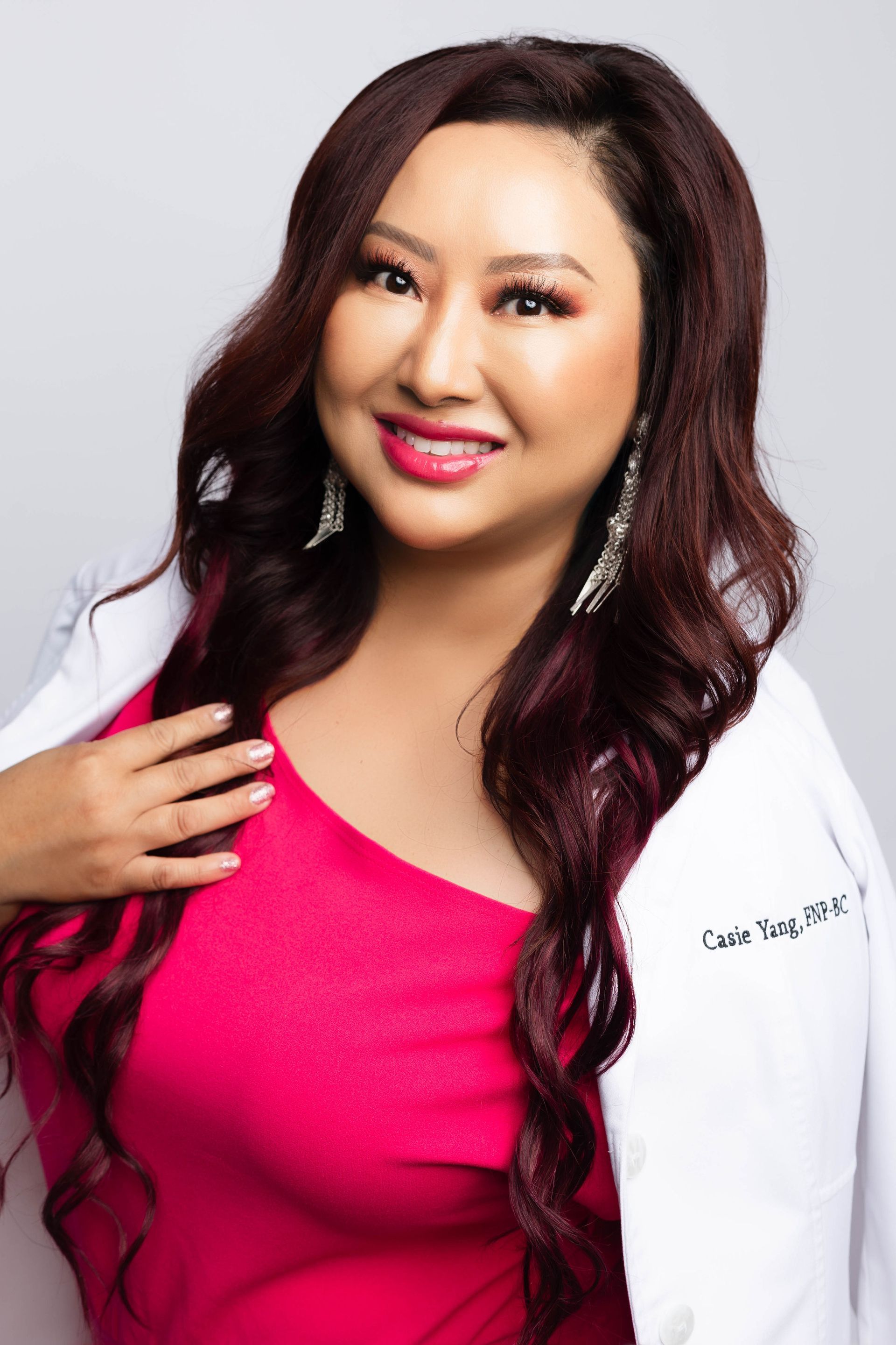 A woman with long red hair is wearing a pink shirt and a white coat.