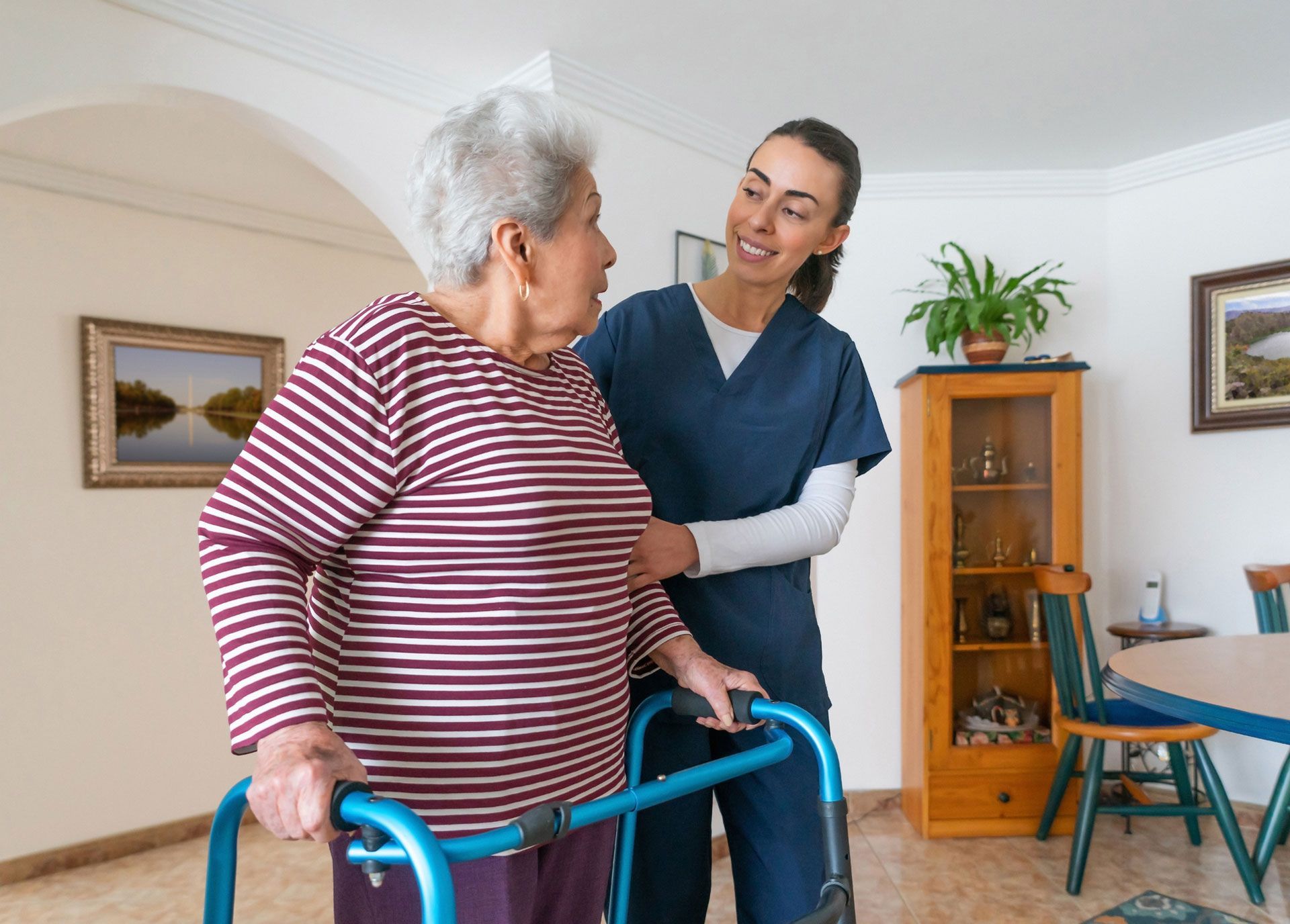 Caregiver assisting elderly woman with walker indoors.