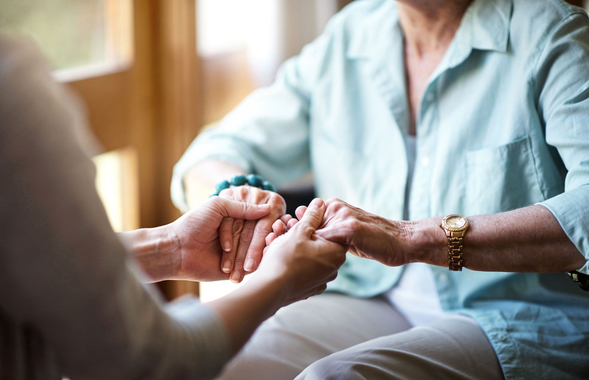 Two people hold hands, a young person and an older person, indoors, showing support and care.