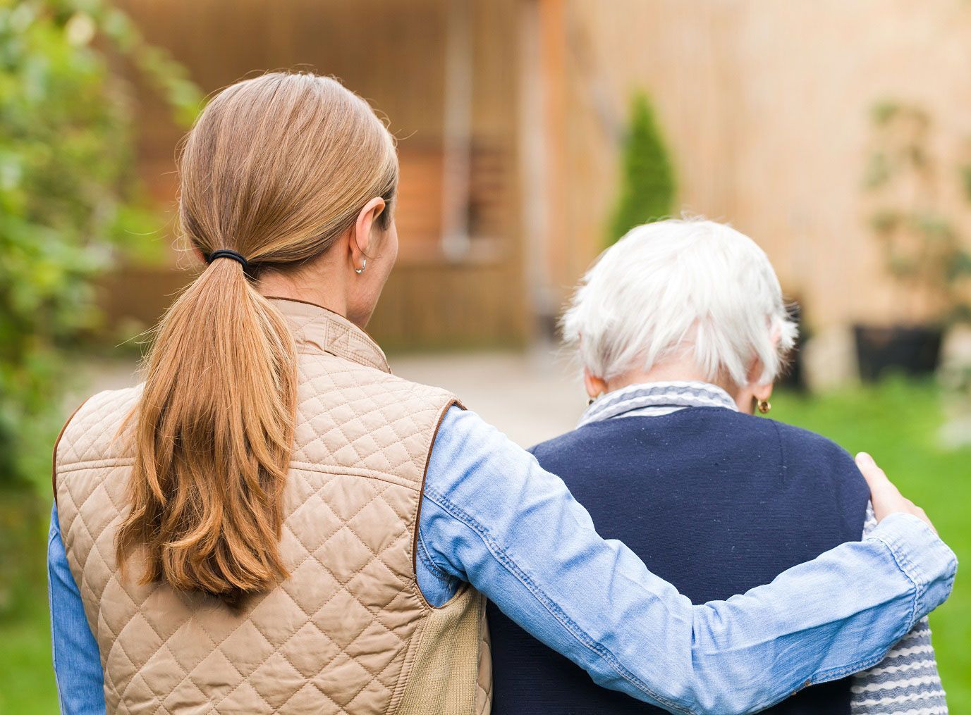 Young woman with arm around elderly woman walking outdoors.