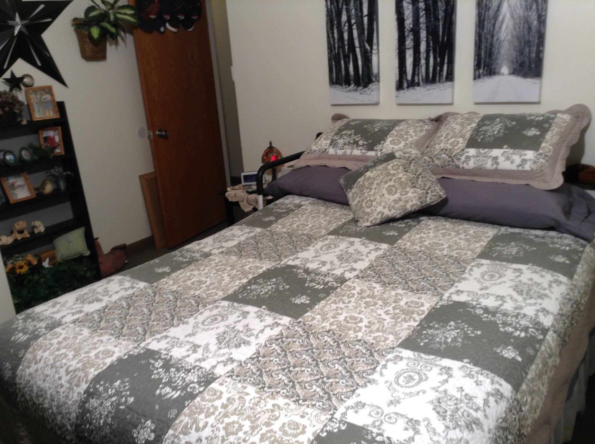 Bedroom with a patchwork quilt in shades of gray, decorative pillows, and artwork on the wall.