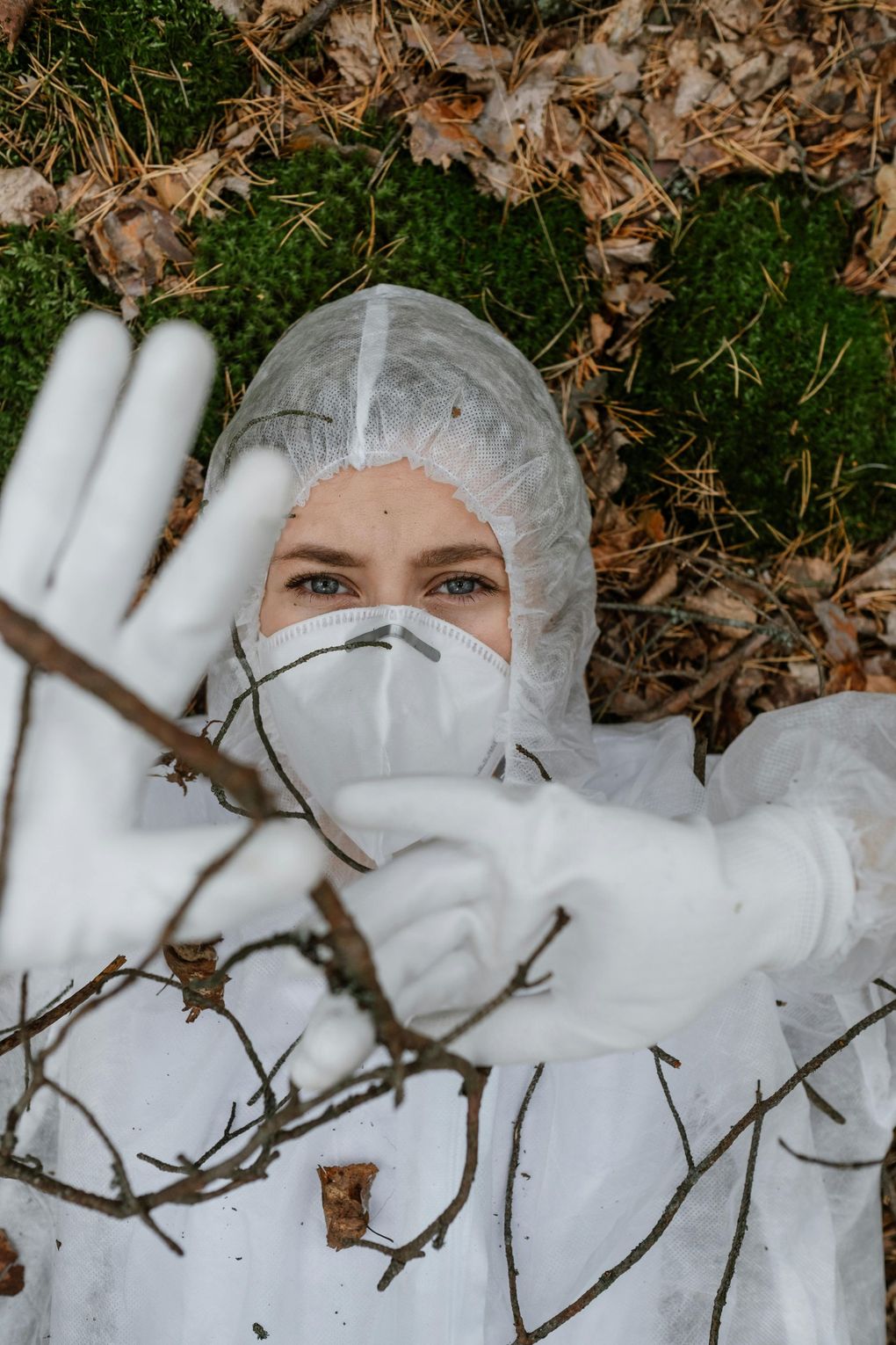 Person wearing blue gloves holding spray bottles, with a yellow cloth and bucket on a surface.