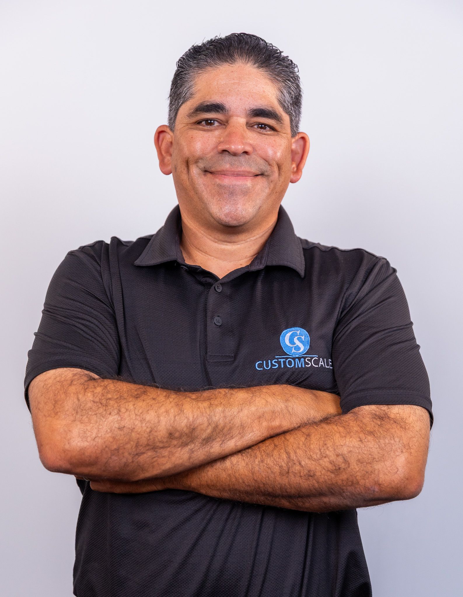 Man with crossed arms, wearing black shirt with logo, smiling against a white backdrop.