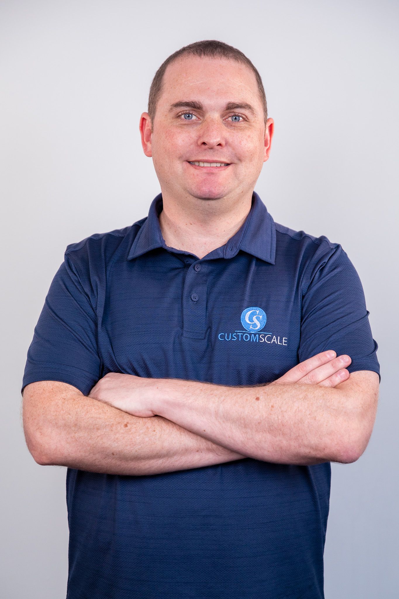 Man with arms crossed, wearing a blue shirt with logo, smiling at the camera.