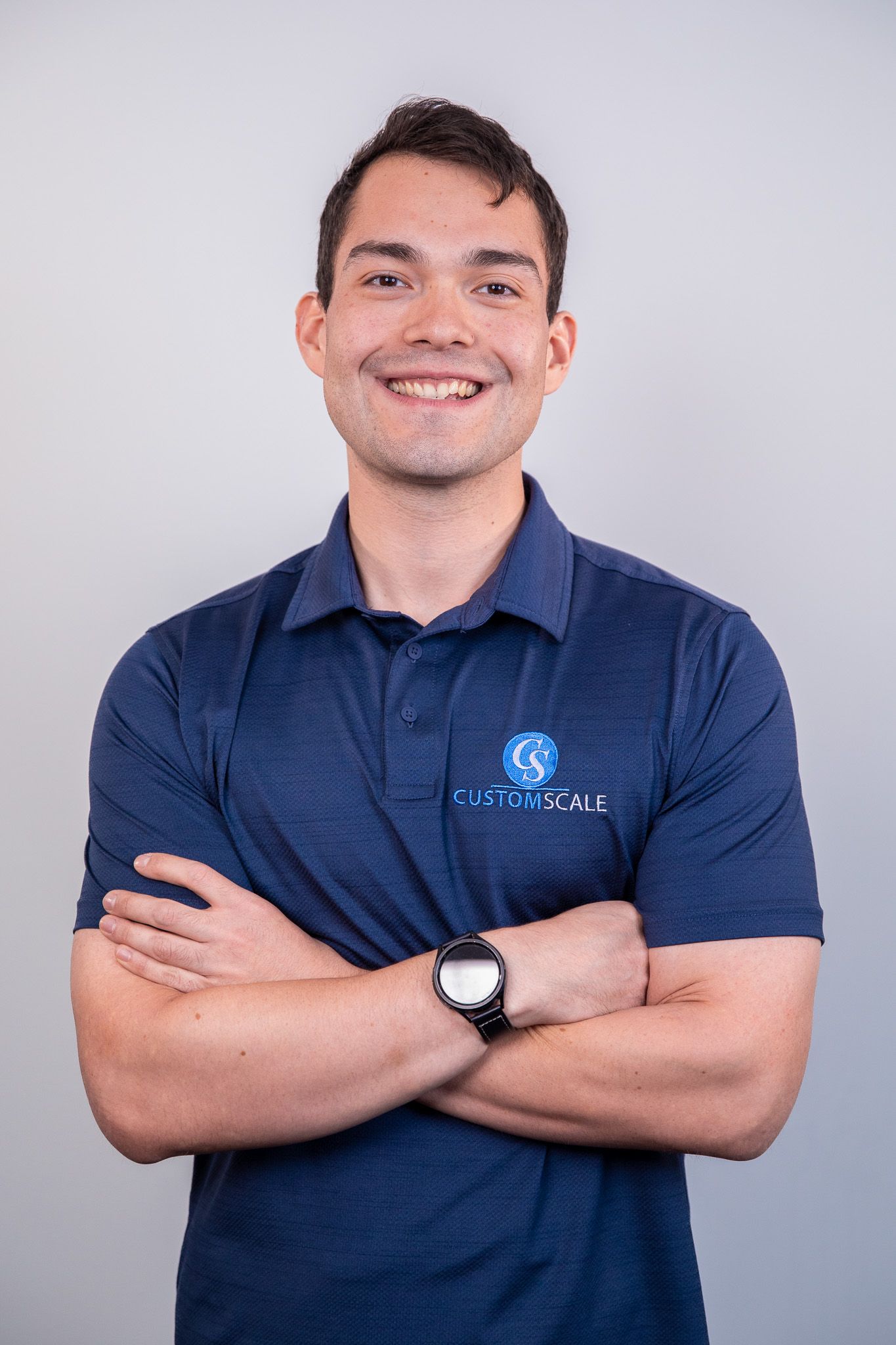 Man with arms crossed, smiling, wearing a blue polo shirt with a logo.