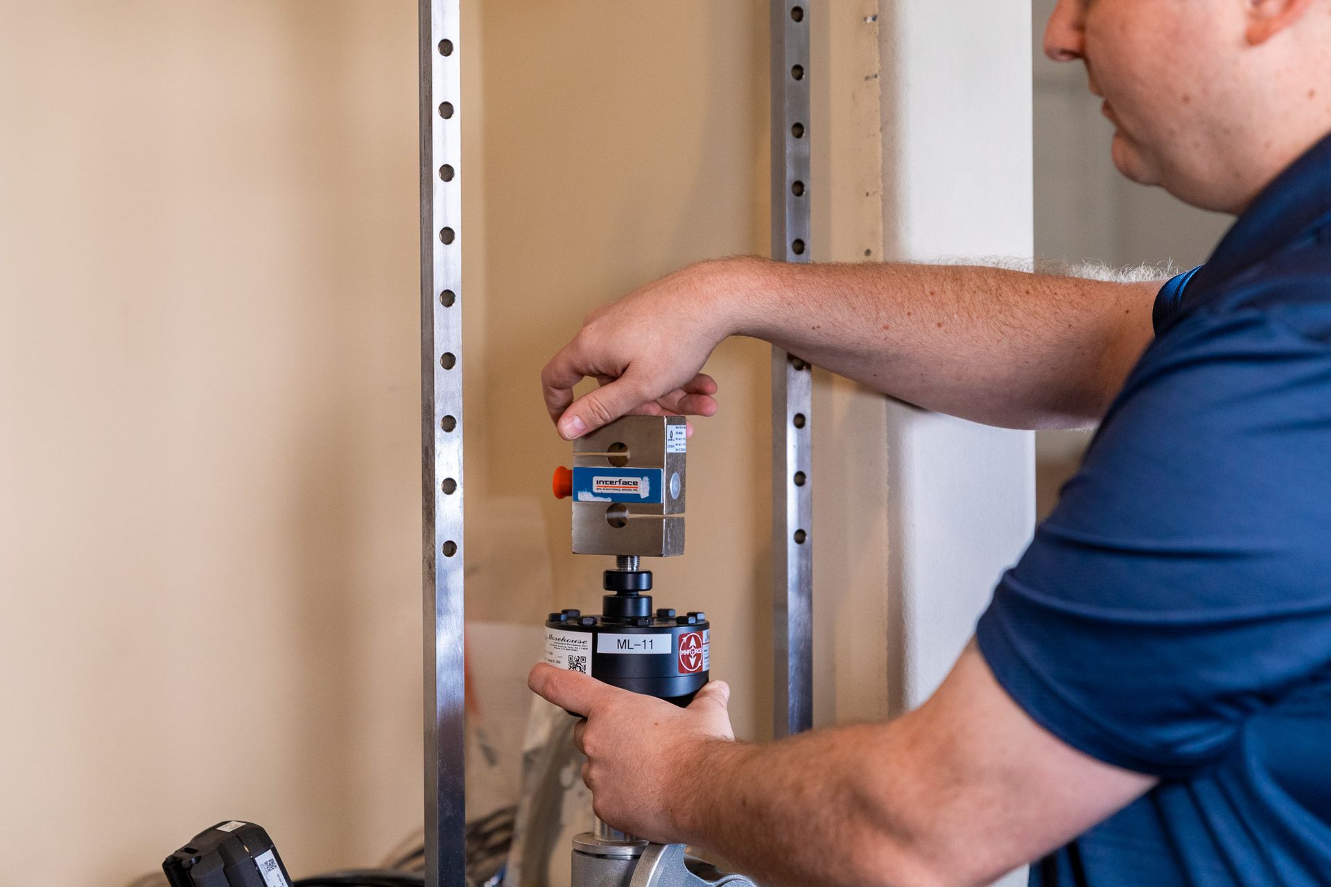 Man assembling machinery, in front of a metal frame on a wall.