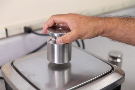 Hand placing a cylindrical metal weight on a digital scale.