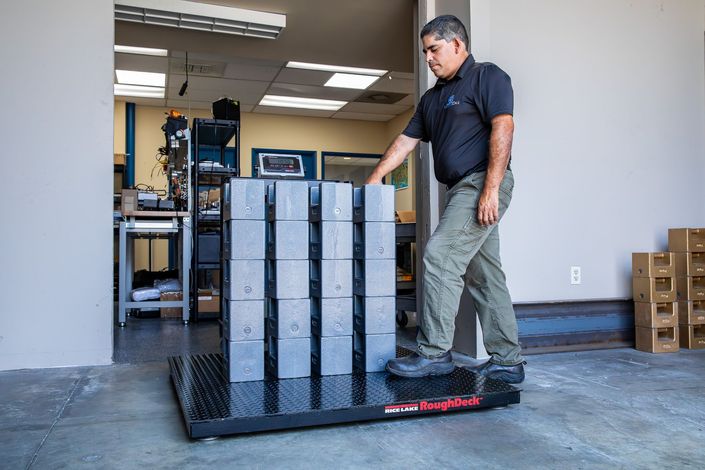 Man pushes a pallet jack loaded with grey blocks out of a doorway.