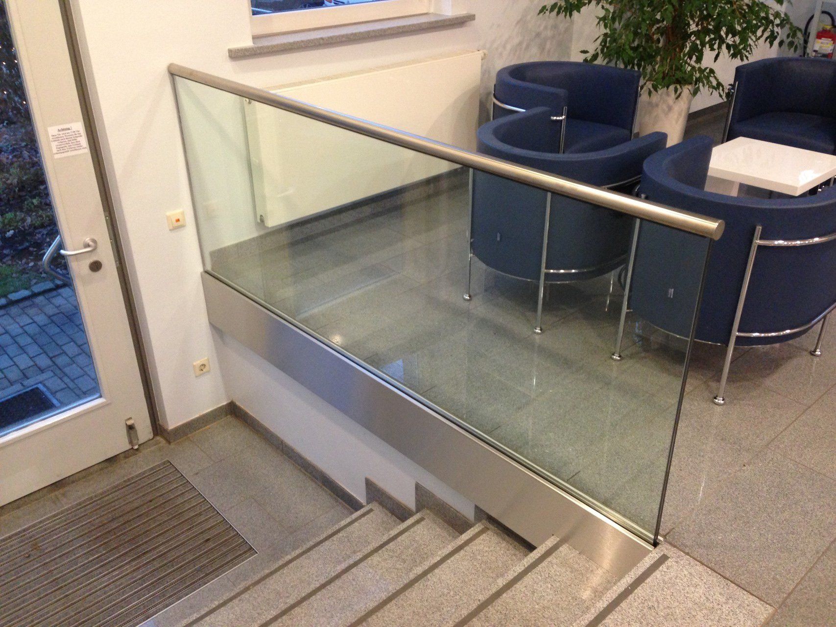 Eine Treppe mit Glasgeländer und blauen Stühlen