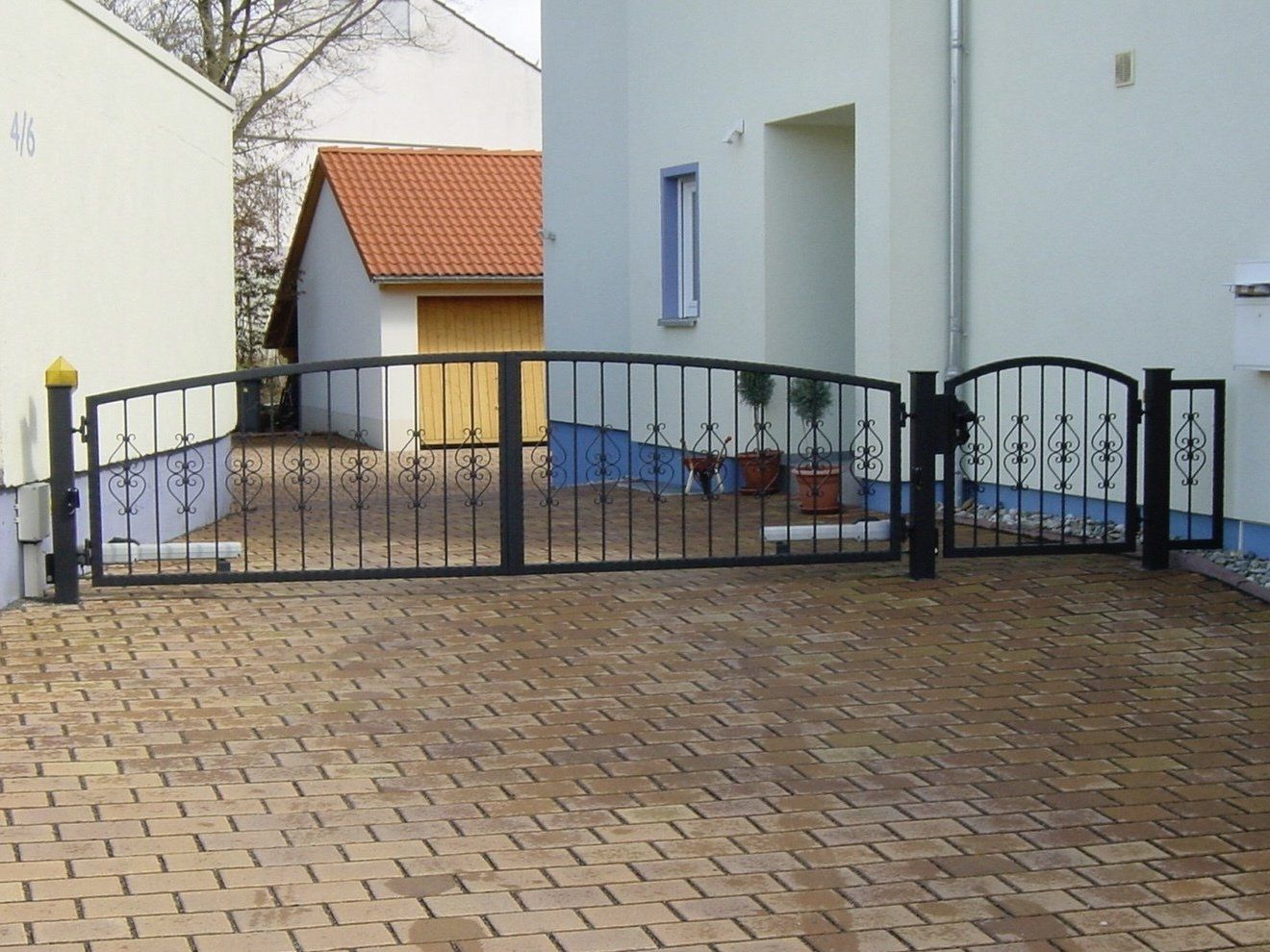 Eine gemauerte Auffahrt mit einem schmiedeeisernen Tor vor einem Haus