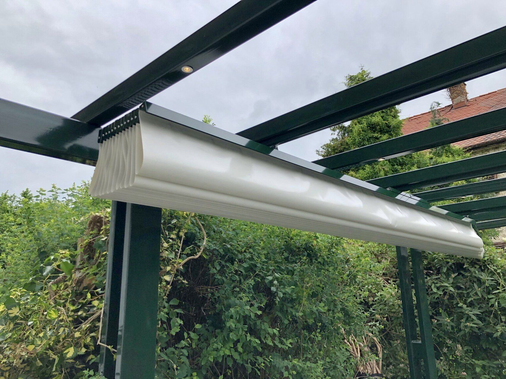 Eine grüne Pergola, von der eine weiße Markise herabhängt.