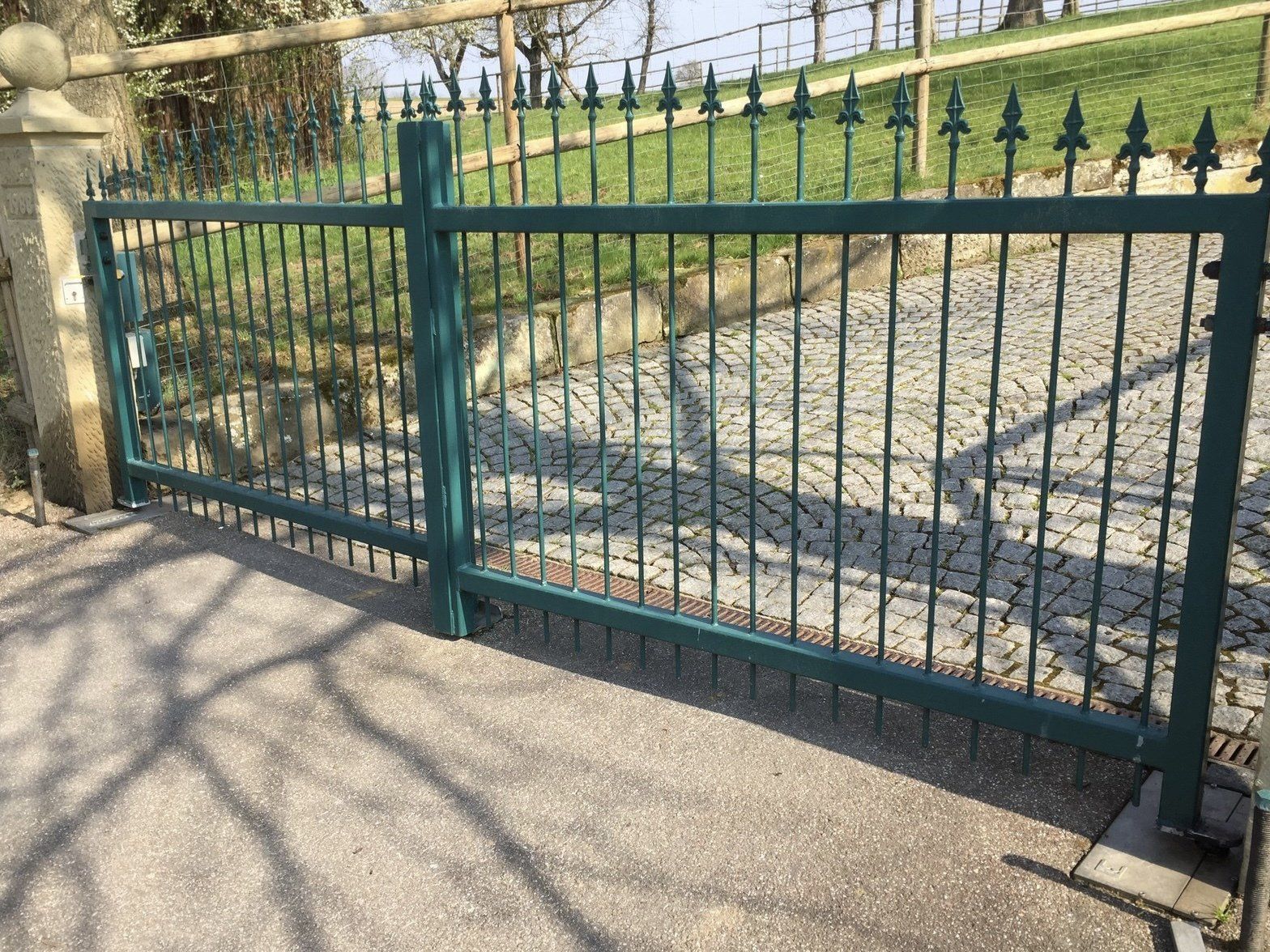 Am Straßenrand steht ein grünes schmiedeeisernes Tor.