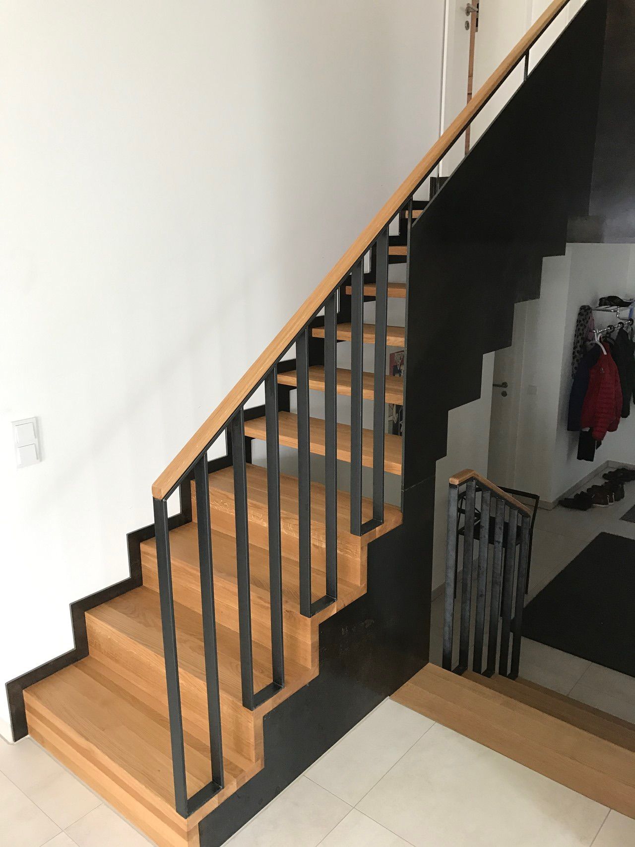 Eine Holztreppe mit einem schwarzen Geländer in einem Flur.