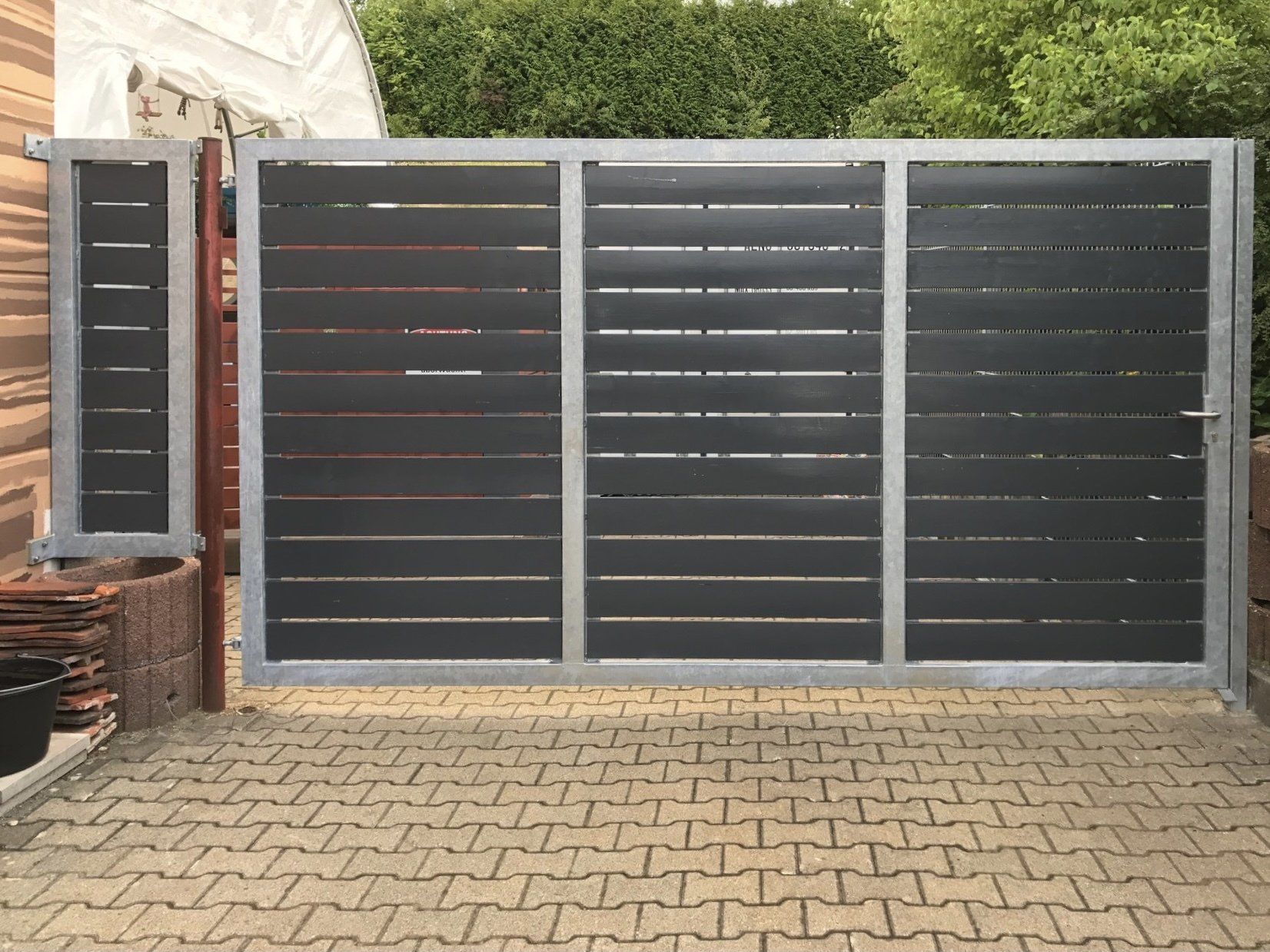 Auf einer gepflasterten Auffahrt steht ein schwarz-silbernes Tor.