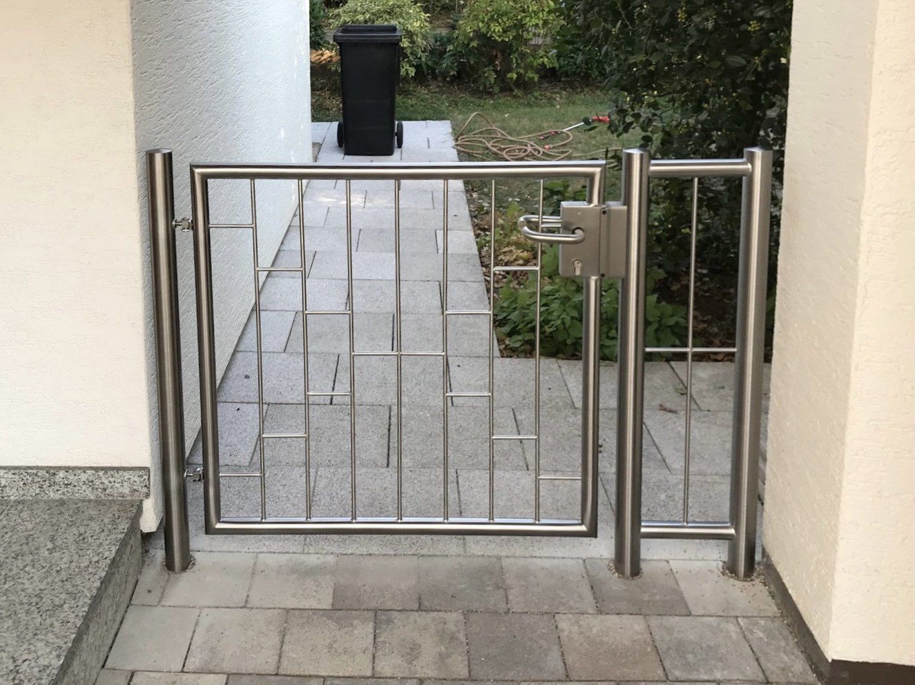 Ein Edelstahltor mit einem schwarzen Mülleimer im Hintergrund