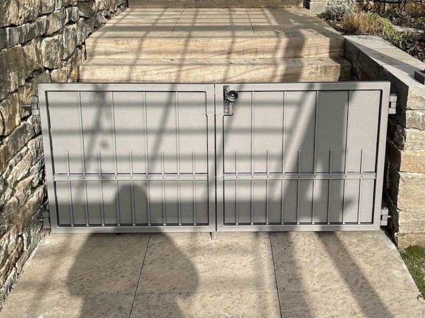 Auf einem Gehweg neben einer Steinmauer steht ein Metalltor.