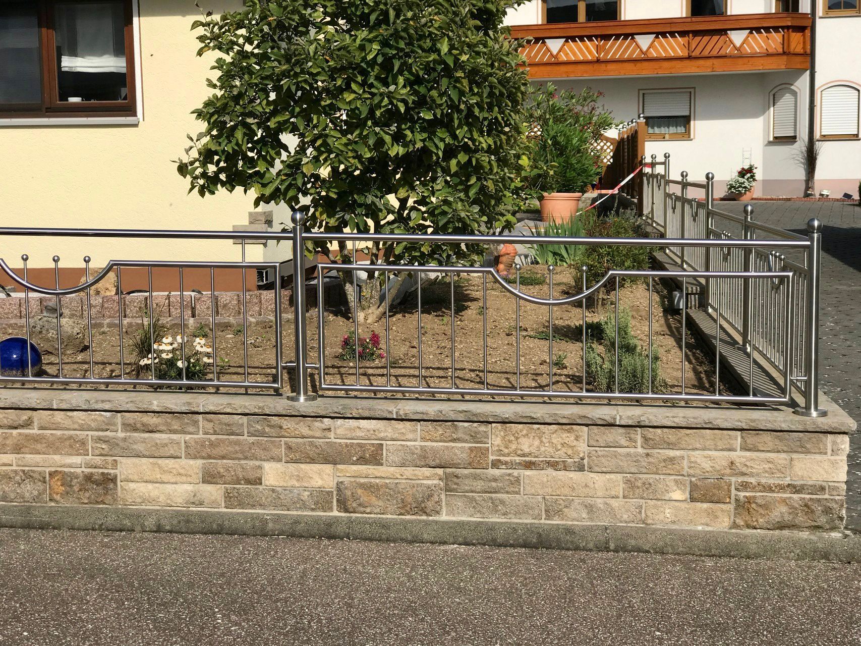 Eine Backsteinmauer mit einem Edelstahlgeländer vor einem Haus.