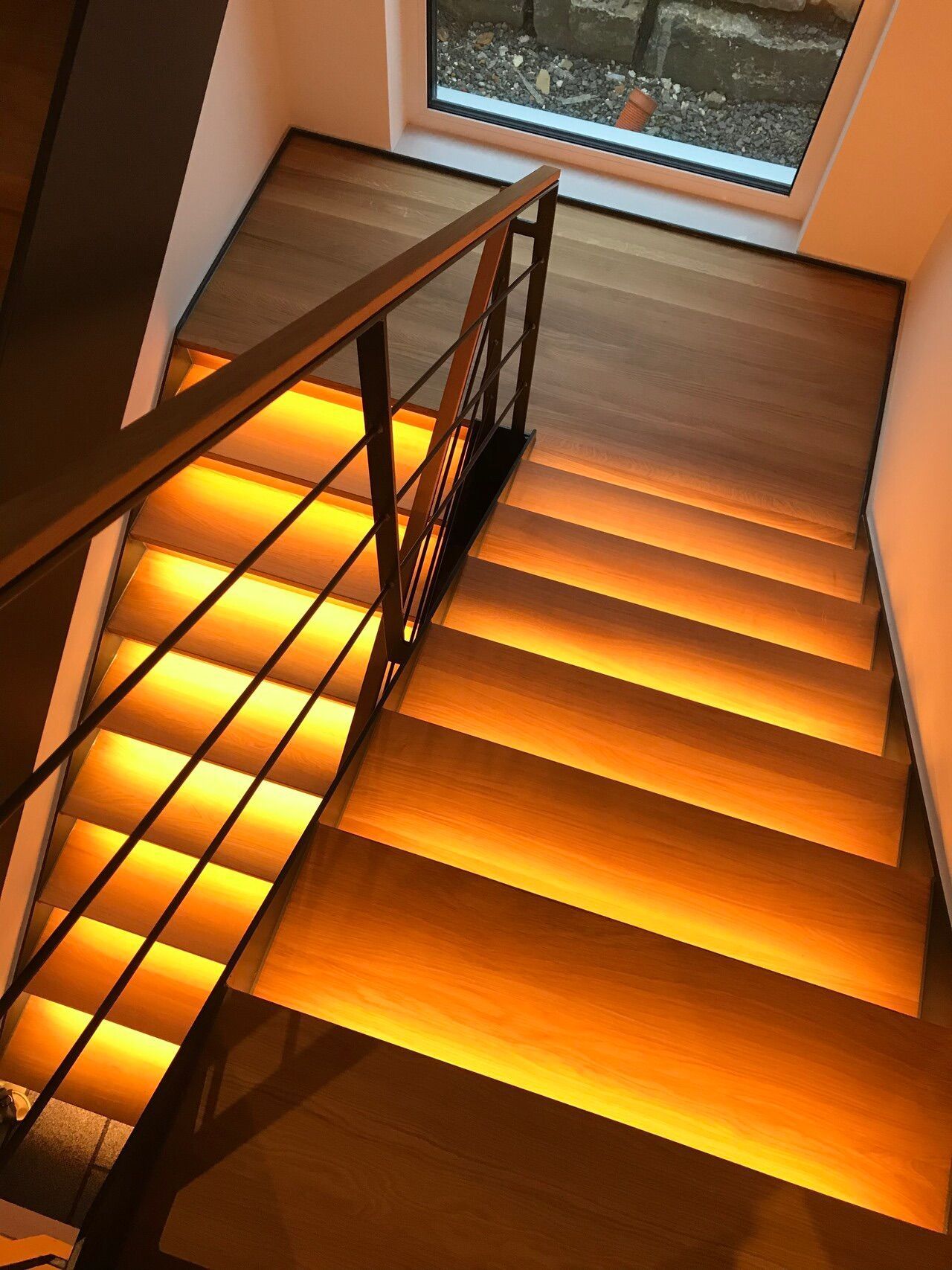 Eine Holztreppe mit einem Metallgeländer und Lichtern auf den Stufen