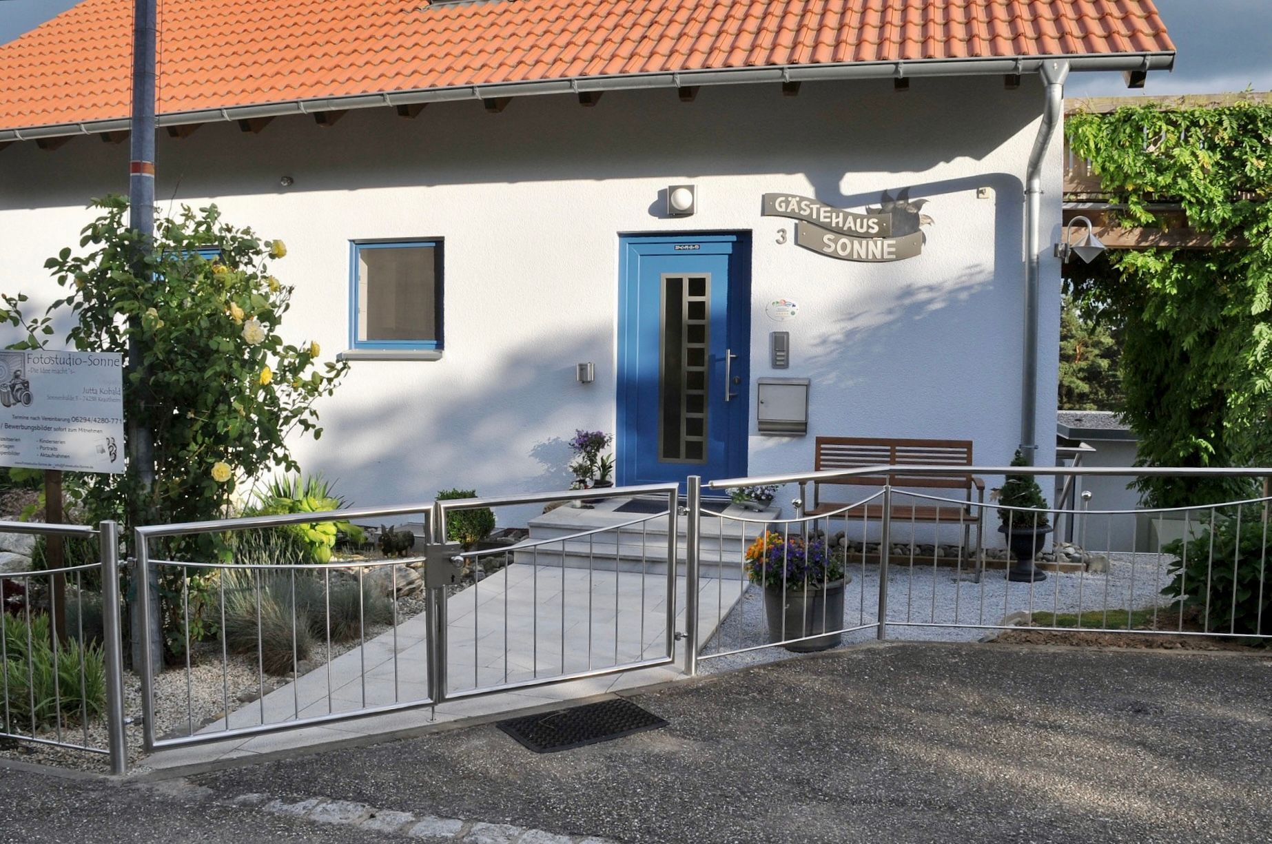 Ein weißes Haus mit einer blauen Tür befindet sich hinter einem Metallzaun