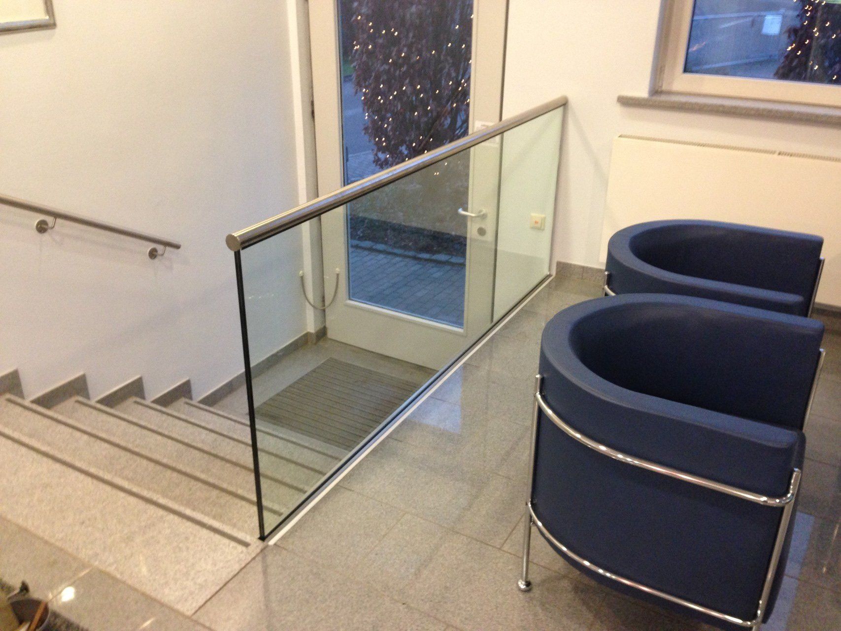 Eine Treppe mit einem Glasgeländer und zwei blauen Stühlen