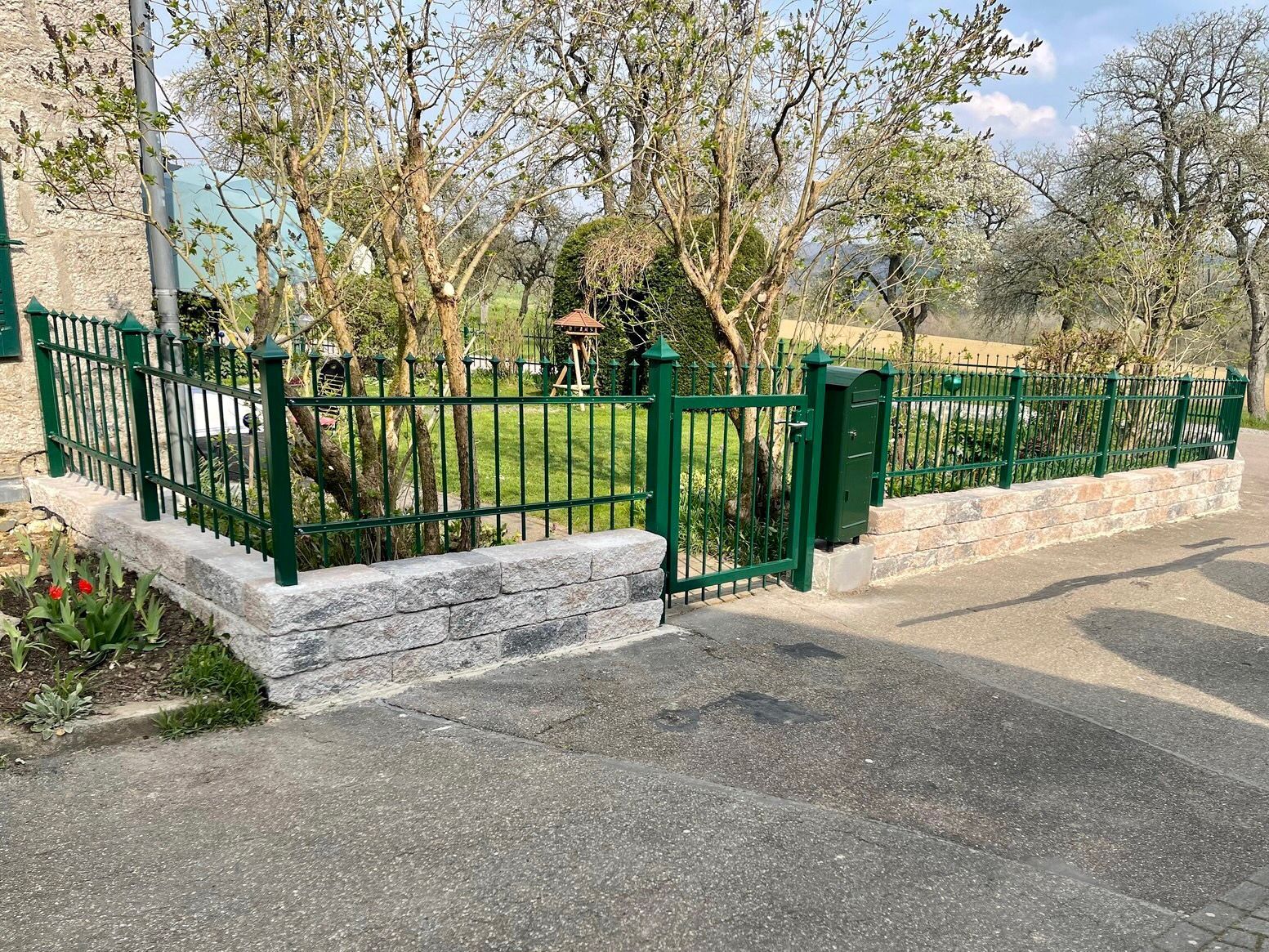 Ein grüner Zaun mit einem Tor vor einem Haus.