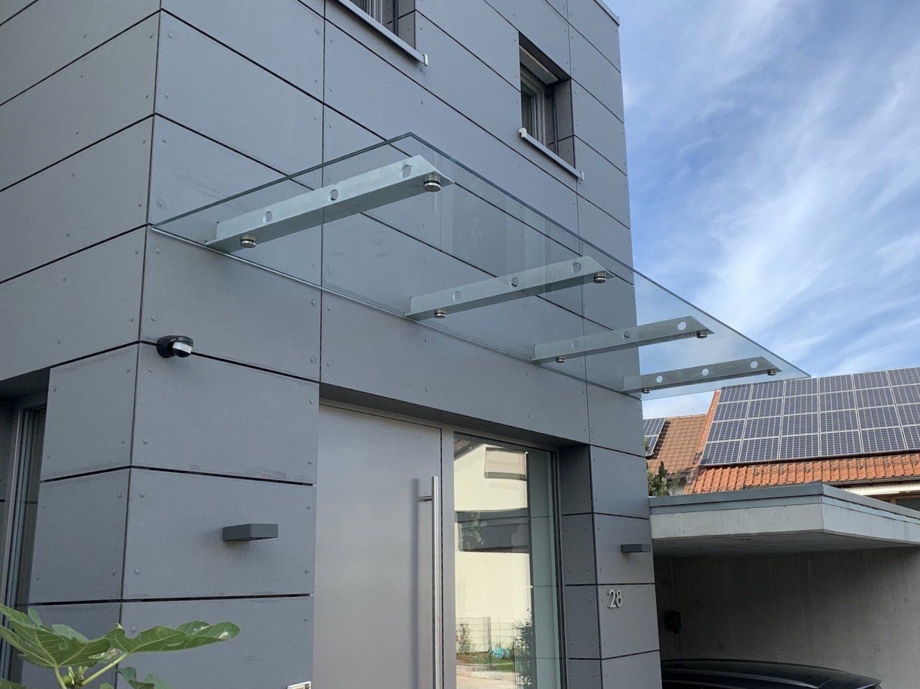 Ein Haus mit einem Glasdach über der Tür und einem darunter geparkten Auto.