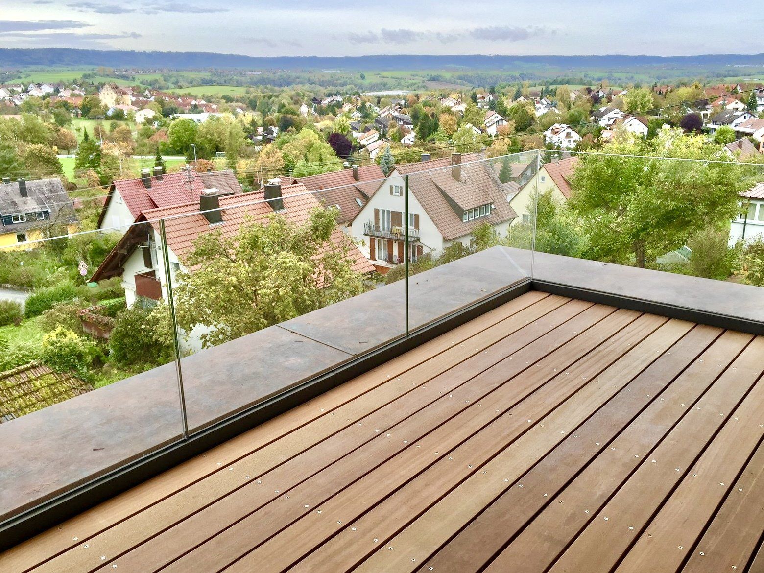 Ein Holzdeck mit Glasgeländer und Blick auf die Stadt.