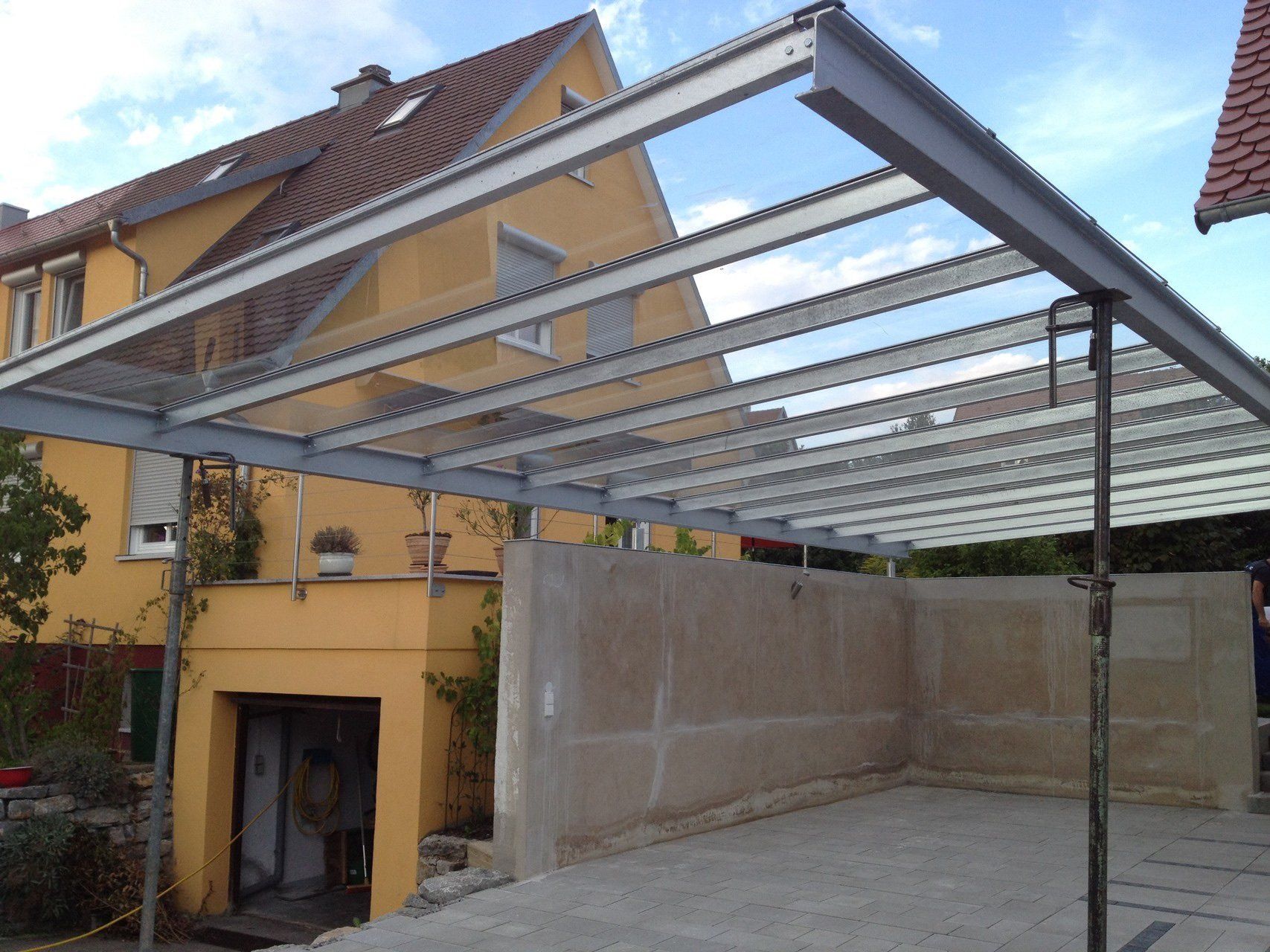 Ein Carport mit Glasdach vor einem gelben Haus