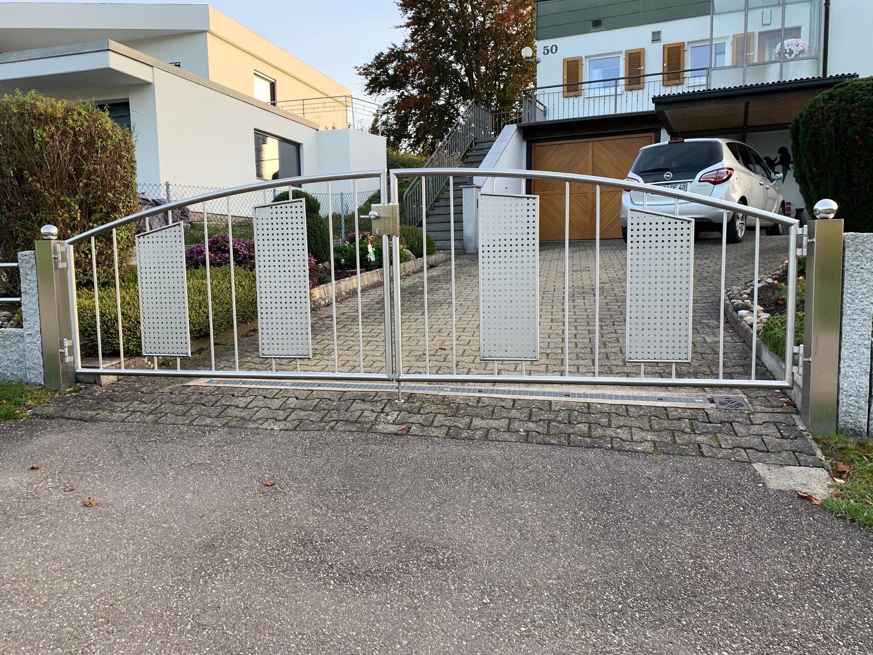 Vor einem Edelstahltor ist ein Auto geparkt.