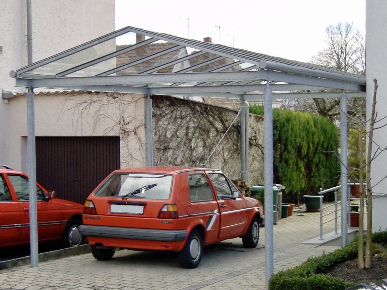 Ein orangefarbenes Auto ist unter einem Carport vor einem Haus geparkt